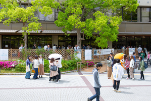 建物前の広場でキャラクターの着ぐるみと人々が交流している写真