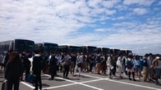 青空に鱗雲が広がる中、大型バスの前に大勢の人が集まっている写真