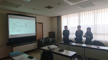 プロジェクターのスクリーンを前に、3人が並んで発表している写真