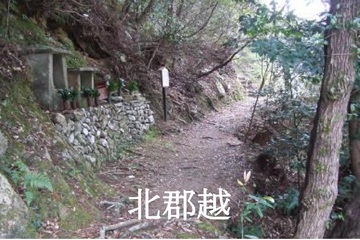 「北郡越」とテキストの入った、山道の狭い道に石造りの祠が建てられている写真(田辺市へリンク)