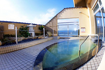 ガラスの向こうに海が見えるタイル張りをした屋外温泉の写真