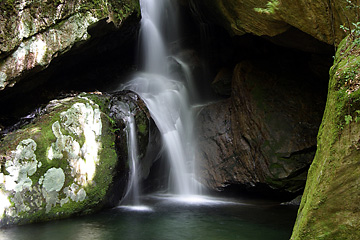 重なり合っている苔のついた岩の間に滝が流れ落ちている写真