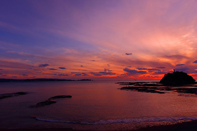 岩礁のある海が夕焼け空に染まっている写真