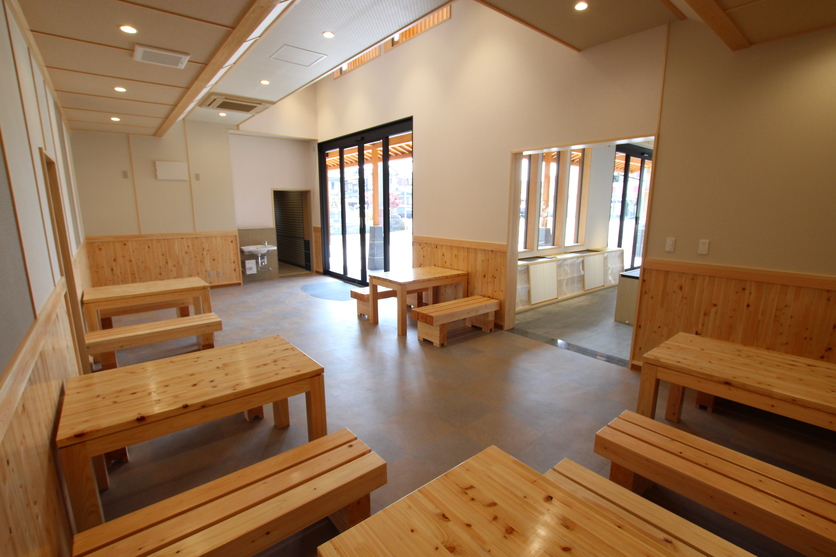 白い壁の部屋に木製のテーブルと長椅子が5セット設置されている写真