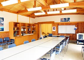 三角の木造天井でホワイトボードやたくさんの机・椅子が並べられた部屋の写真