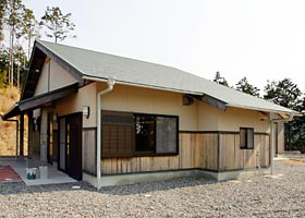 クリーム色の壁に緑の屋根でできた平屋の写真