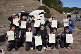 ゆるキャラの前に2列に並んで1人1枚賞状を持って見せている集合写真