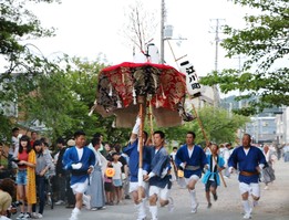 大きな笠に似たお祭りの道具を持って走る法被姿の男性の写真