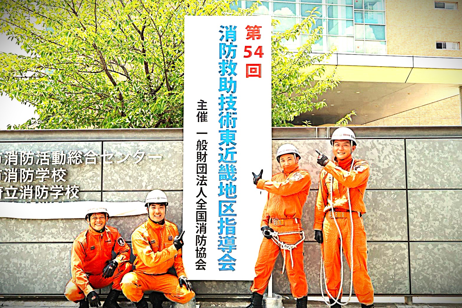 第54回東近畿地区指導会の看板の前に田辺消防の出場選手が並んでいる画像