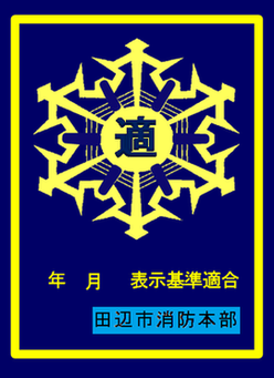 雪の結晶のような黄色のマークの中央に「適」の文字が入り、下部に「表示基準適合 田辺市消防本部」と記された青地の表示マークの写真