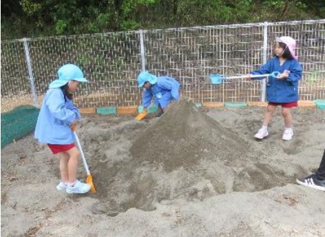 園児が砂場で山を作って遊んでいる写真