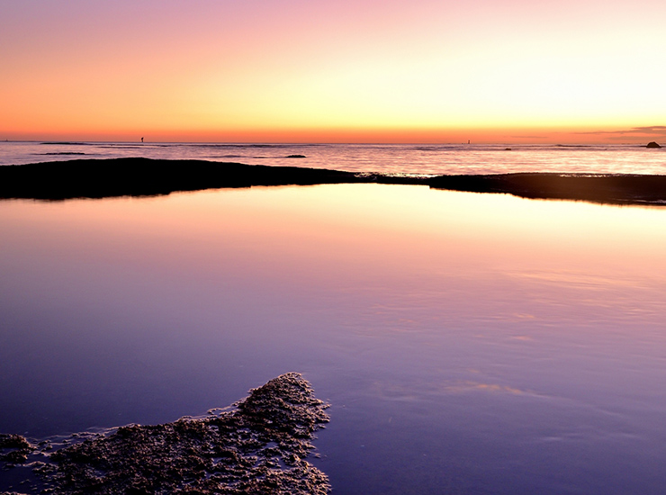 夕焼けに染まる空と岩礁が、水面に鏡のように映り込む田辺市の海岸風景