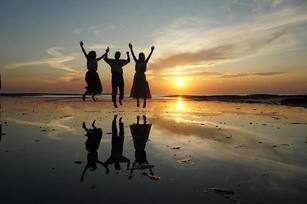 夕日を背に、三人が横並びで手を空にあげてジャンプしている姿が水面に合わせ鏡の様に映し出されている写真