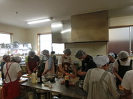 厨房で白い頭巾を着けた複数の人が調理をしている写真