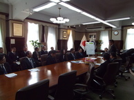 長方形の机に並んで座るスーツを着た男性達の写真