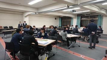 会議室で複数のグループがテーブルを囲んで話し合いを行っている写真