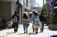 晴れた商店街の歩道を5人の男女が並んで歩いている写真