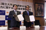 スーツを着た男性2人が書類を手にして並んでいる写真