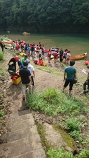 川辺に多数のカヌーが並び、ライフジャケットを着た人々が集まっている写真