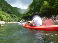 山あいの川で赤いカヌーに乗った2人が川下りをしている写真