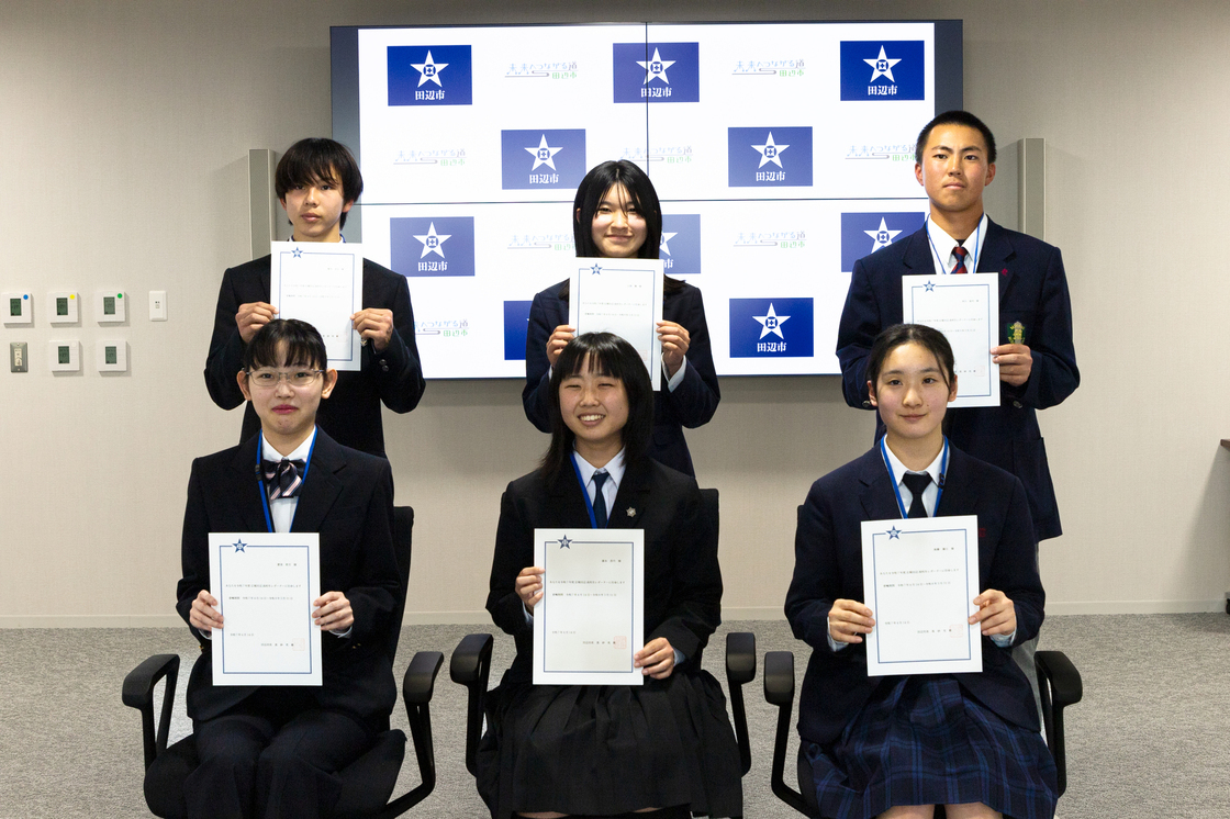 紙を持った男女の生徒6人が前後2列に並んでいる写真