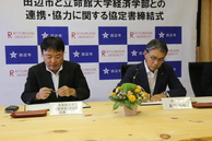 スーツを着た男性2人が座って書類に書き込んでいる写真