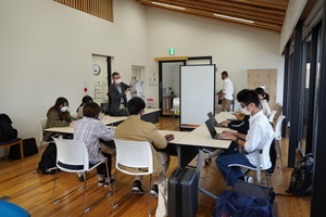 コの字型のテーブルでノートパソコンを使って作業している人達の写真