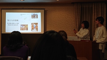 暗めの会議室で、スクリーンを使って2人の女性が発表している写真