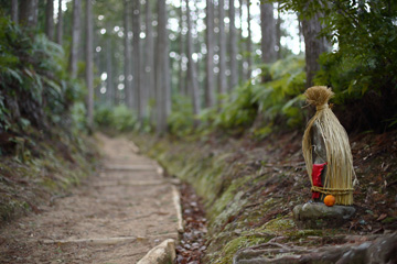 山道に藁をかぶった小さなお地蔵様が置いてある写真