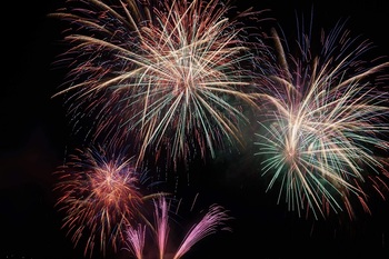 真っ暗な夜空の中にピンク・赤・緑・白などの色鮮やかな花火が打ち上げられている写真