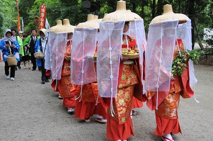 笠をかぶり装束を身にまとった女性たちが梅の実うぃ奉納している写真