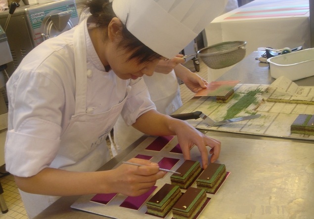 コック帽を身に付けた女性がケーキの上に金箔を乗せている写真