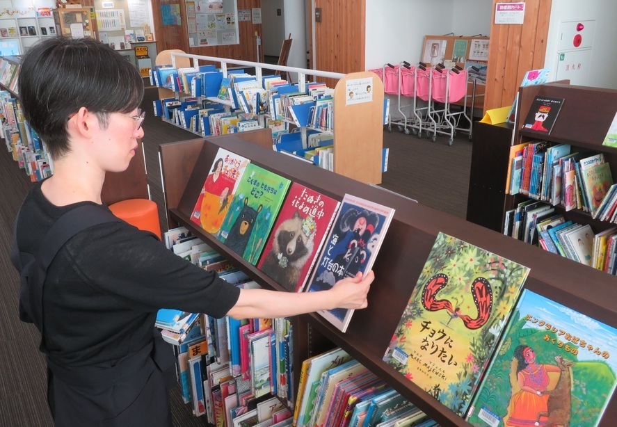 本棚に絵本を並べている人の写真