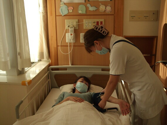 病室のベッドに寝ている人の腕を触っている看護師の写真