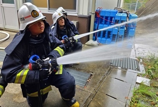 水が噴射しているホースを構える消防服を着た人の写真