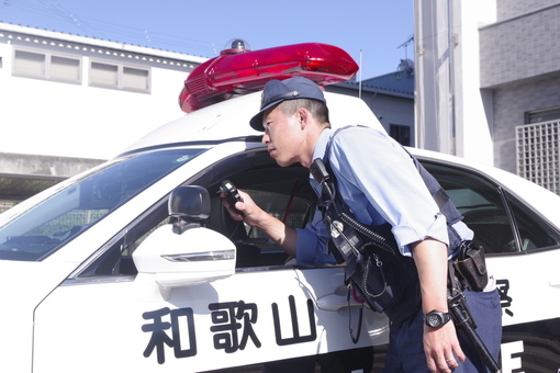 パトカーの外から助手席の窓に肘を置いてマイクを持つ警察官の写真