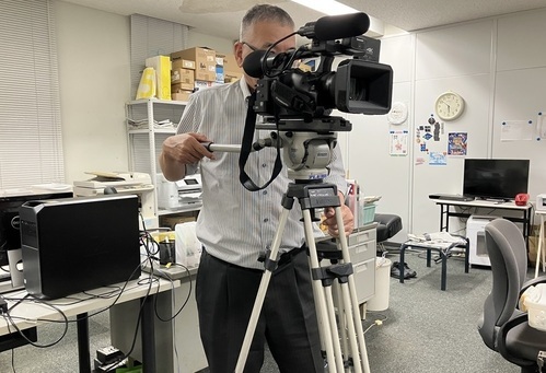 三脚に固定された業務用カメラを操作している男性の写真