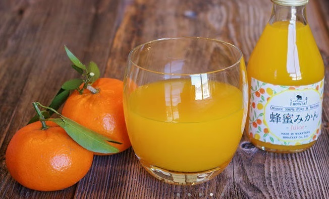 ミカンジュースが入ったコップの横にみかん2個とビンが置かれた写真