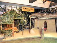 屋内に展示された、細い木を組み合わせてできた簡易的な2つの小屋の写真