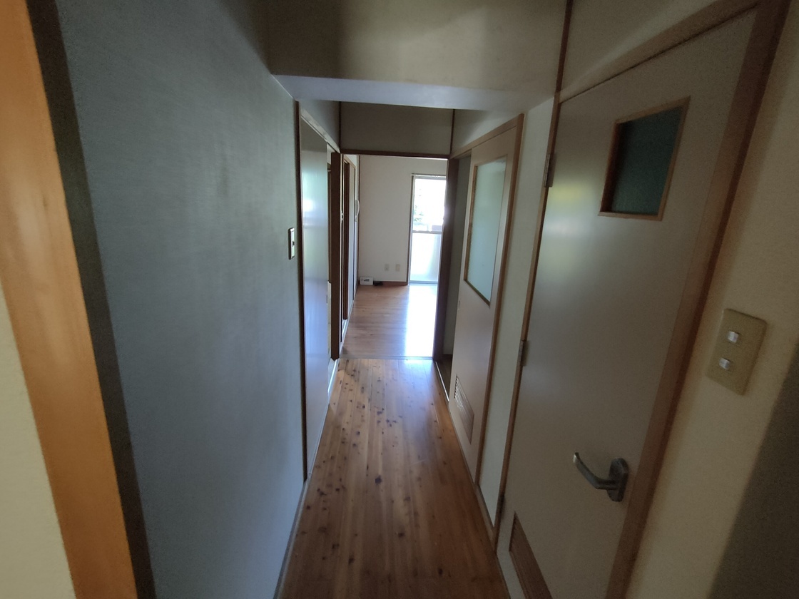 両側と突き当りに部屋が複数あり突き当りの部屋のドアが開いてる廊下の写真