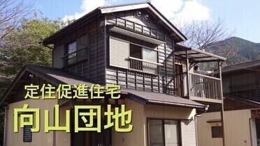 2階建ての家屋を背景に「定住促進住宅 向山団地」と書かれた写真