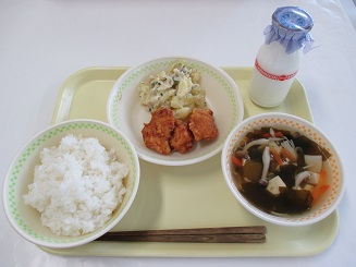 ごはん、ジャーマンポテトと揚げ物、わかめスープと牛乳が置かれたお盆の写真