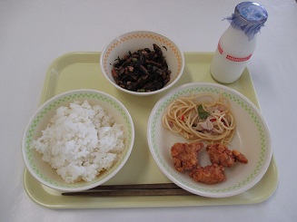 ごはん、ひじき、パスタと唐揚げと牛乳が置かれたお盆の写真