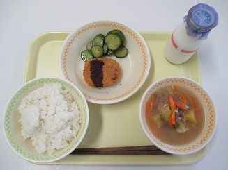 ごはん、きゅうりとコロッケ、スープと牛乳が置かれたお盆の写真