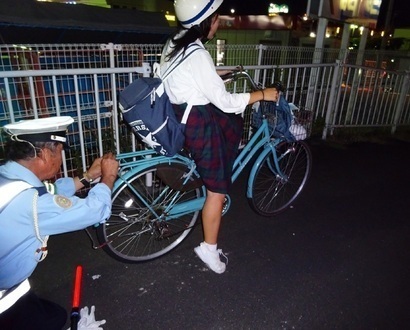 夜の道路脇で学生が乗っている自転車に警察官が反射材を取り付けている写真
