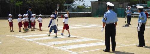 553運動場に白線で引いた横断歩道で渡り方の練習している体操服を着た児童たちの写真