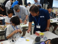 席で工作をする子供の手元を見ている男性の写真