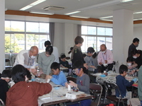 席で工作をする子供たちに指導をする数名の大人たちの写真