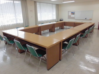 ロの字に置かれたテーブルに椅子がしまわれている会議室の写真