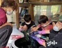 ゴム手袋をして作業する男の子3人を見守る男性の写真